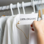 T-shirt made of 100% and hundred percent organic materials. Customer with responsible and nature and eco friendly values looking for clothes in store or shop. Holding label and price tag with text.